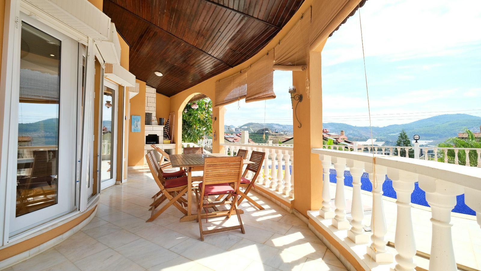 Spacious covered terrace at a villa with wooden table, arched openings and mountain views