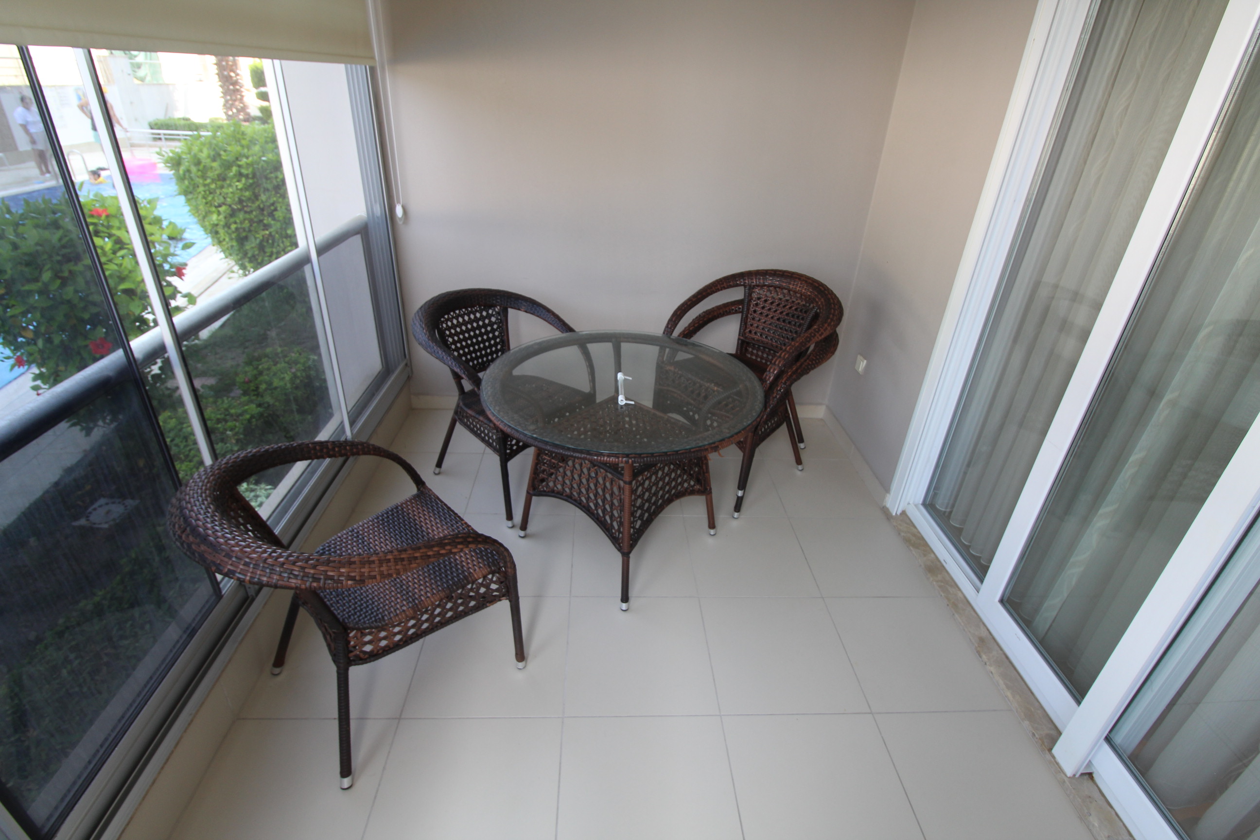 Hasır koltuklu balkon Türkiye’de satılık konutta cam arkasındaki havuza bakıyor