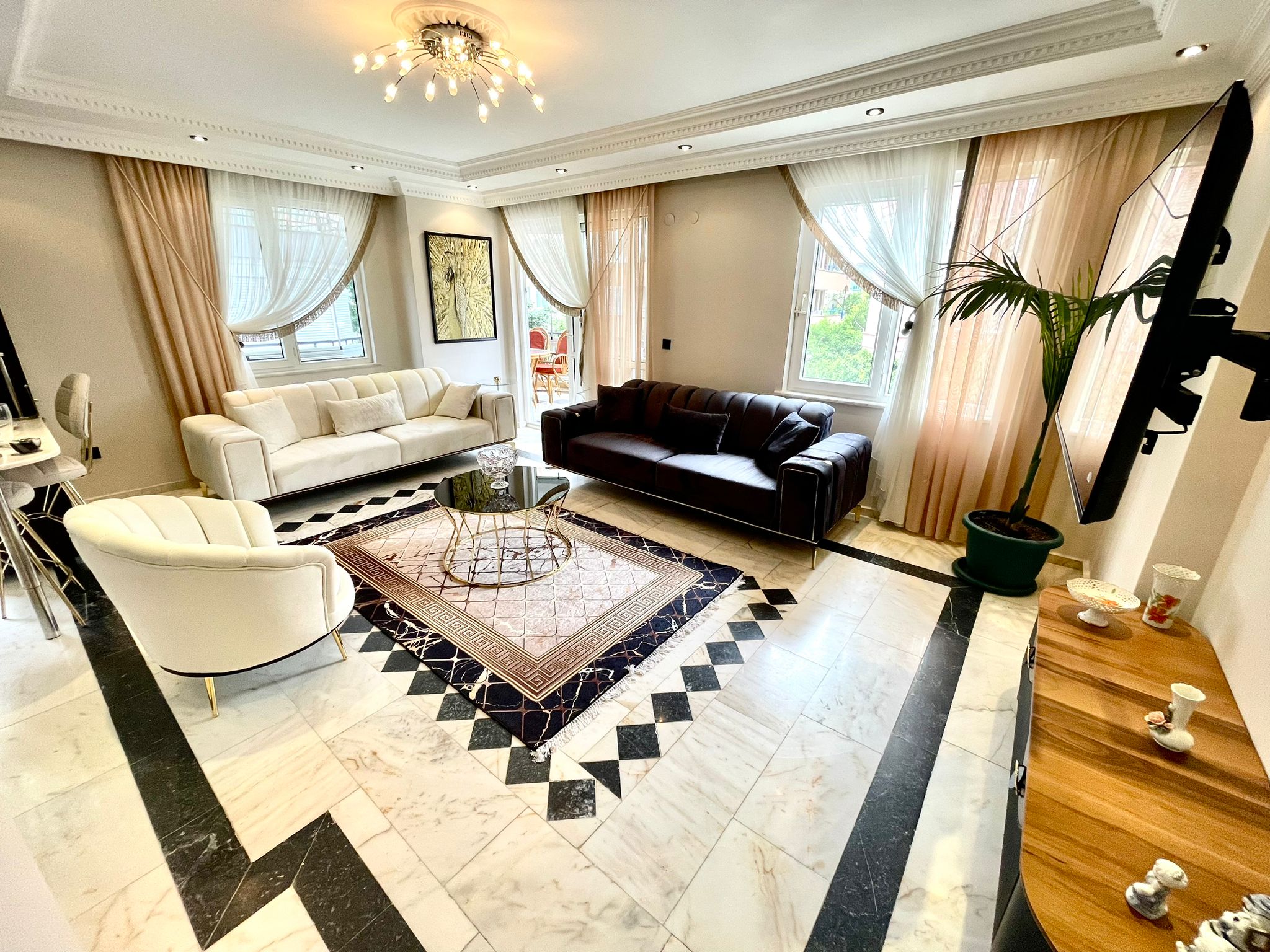 Oba'daki 2+1 dairenin salonunda beyaz ve lacivert koltuklar, panoramik pencereler ve balkon kapısı