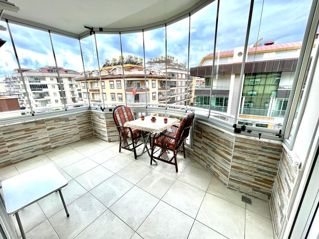 Satılık dairenin camlı balkonunda dört hasır koltuklu yemek masası ve panoramik pencereler