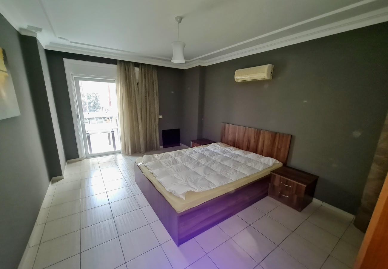 Yatak odasında Oba’daki 2+1 dairenin ahşap başlıklı çift kişilik yatağı ve balkon kapısı
