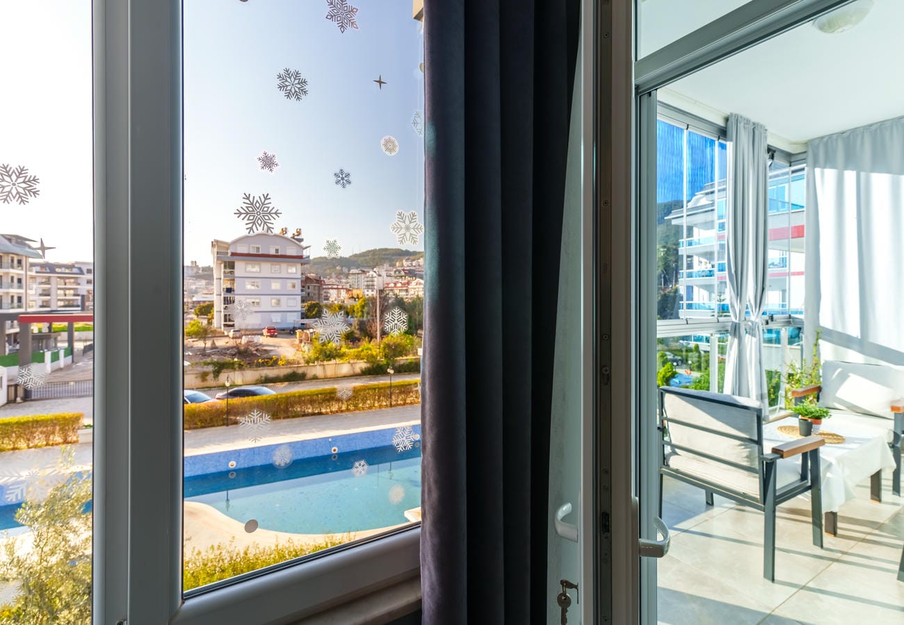 Camla kapalı balkonda gri koltuk, pencere önü bitkileri ve avlu havuzu, Oba’da Türkiye’deki 3+1 dairede