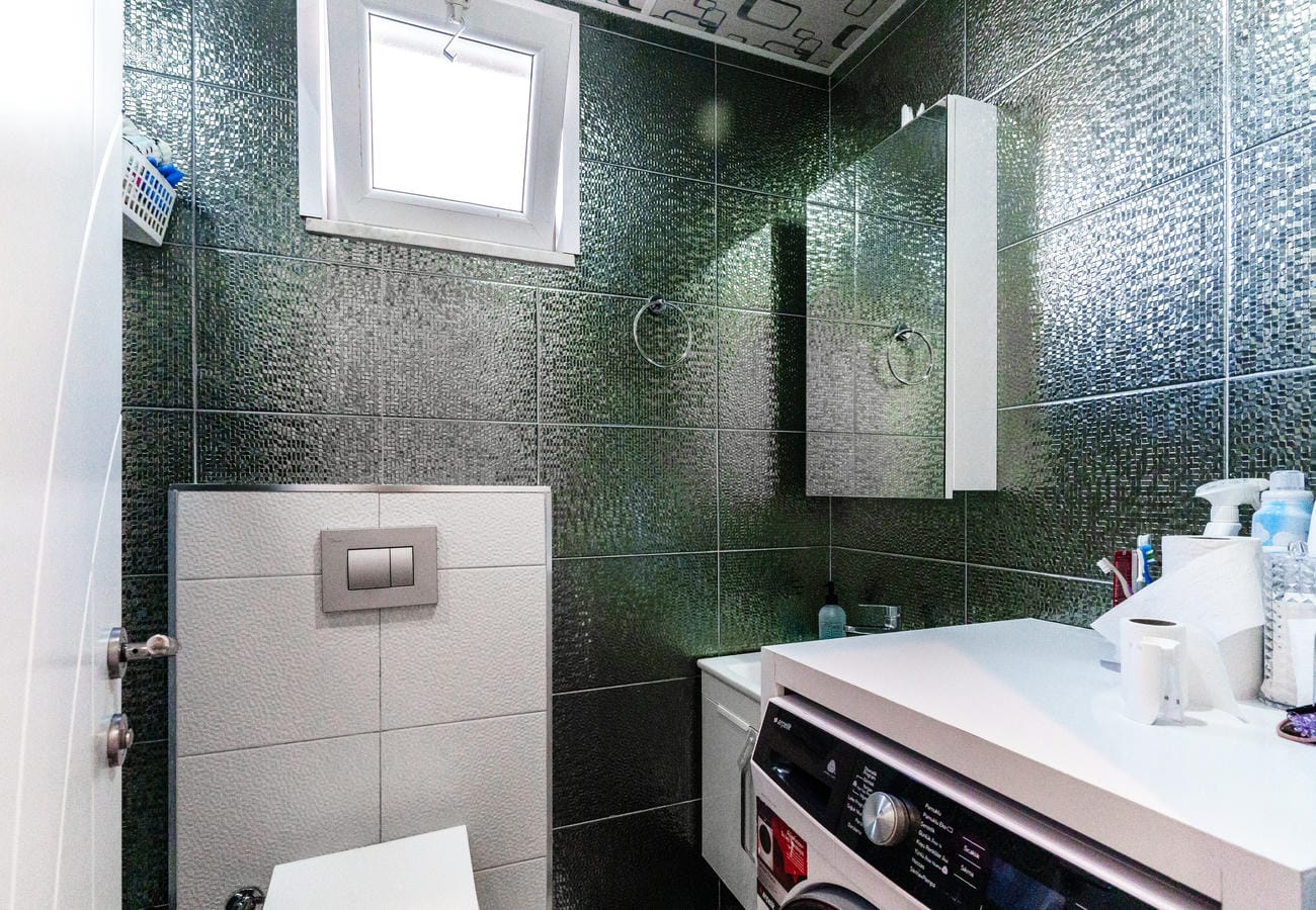 Banyoda uzun tezgâh üstü lavabo, çamaşır makinesi ve koyu mozaik kaplama, Oba’da