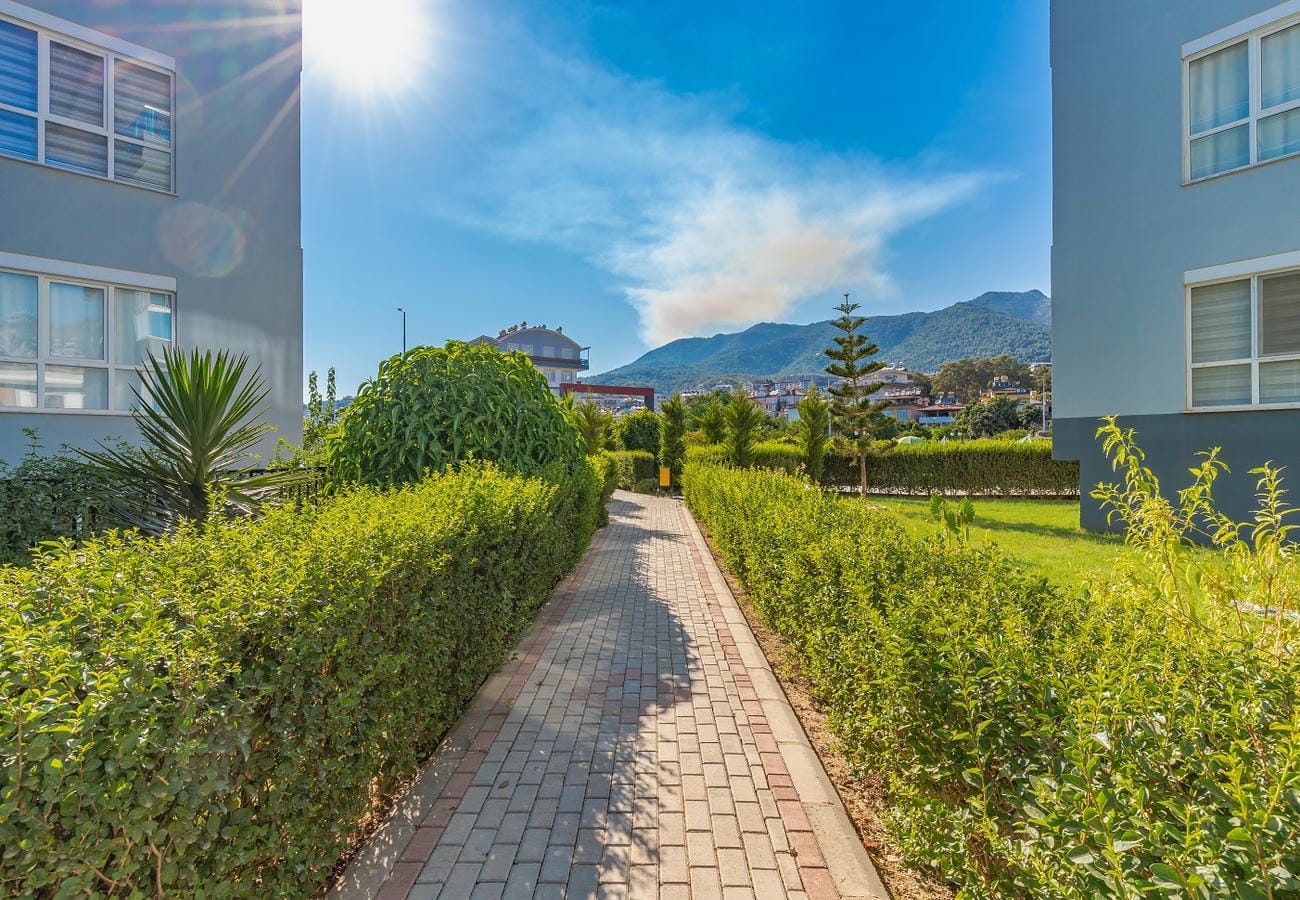 Çimlerin ve çitlerin arasındaki taş döşeli yol, Alanya’da satılık 3+1 dairelerin bulunduğu sitede