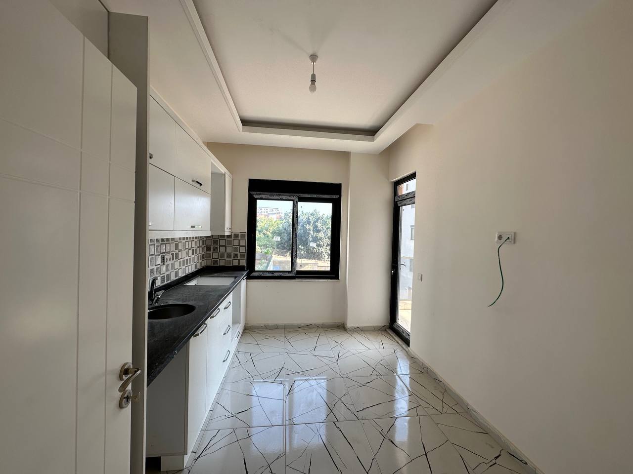Alanya’da mutfakta yuvarlak eviyeli düz beyaz dolaplar ve balkona açılan cam kapı