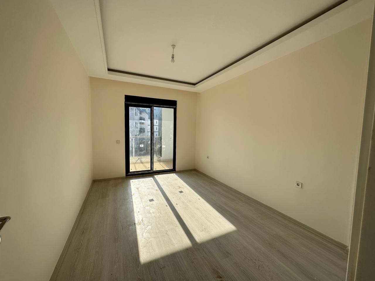 2+1 dairenin salonunda balkona açılan çift cam kapı ve zeminde dikdörtgen güneş ışığı