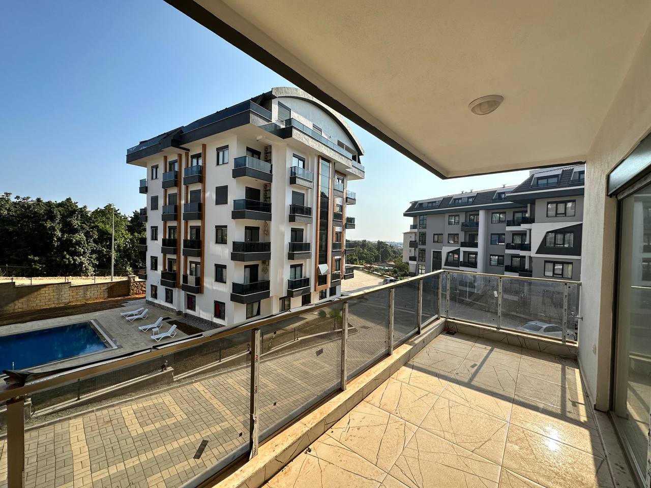 Havuz ve beyaz şezlonglara bakan geniş balkon, Türkiye’de satılık dairenin bej karolarıyla