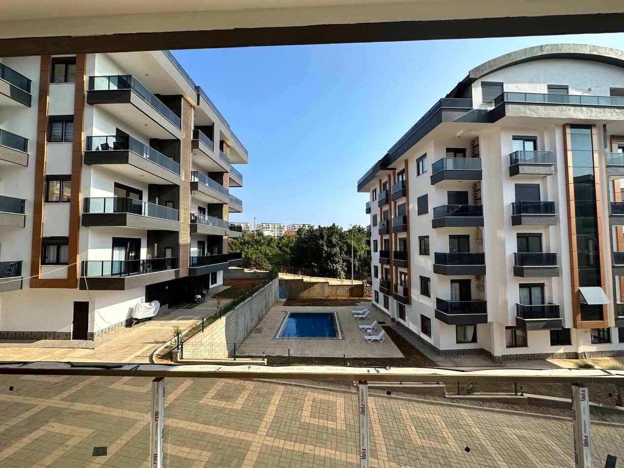 Cam korkuluklu balkon, satılık 2+1 daireden havuz ve şezlonglu avluya bakıyor