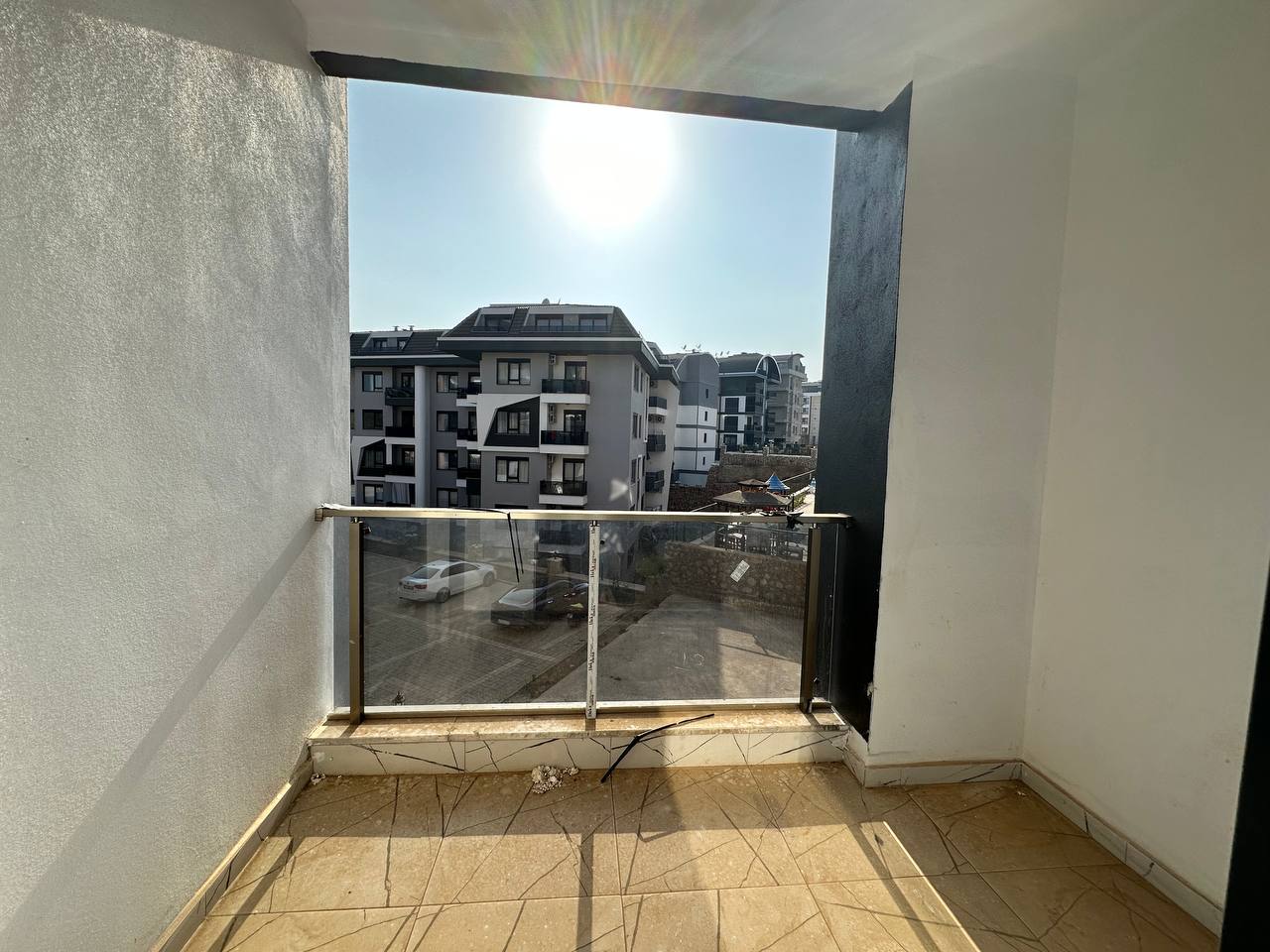 Bej karolu küçük kapalı balkon, Oba’daki dairenin karşı bloklara ve avlu yolundaki araçlara bakıyor