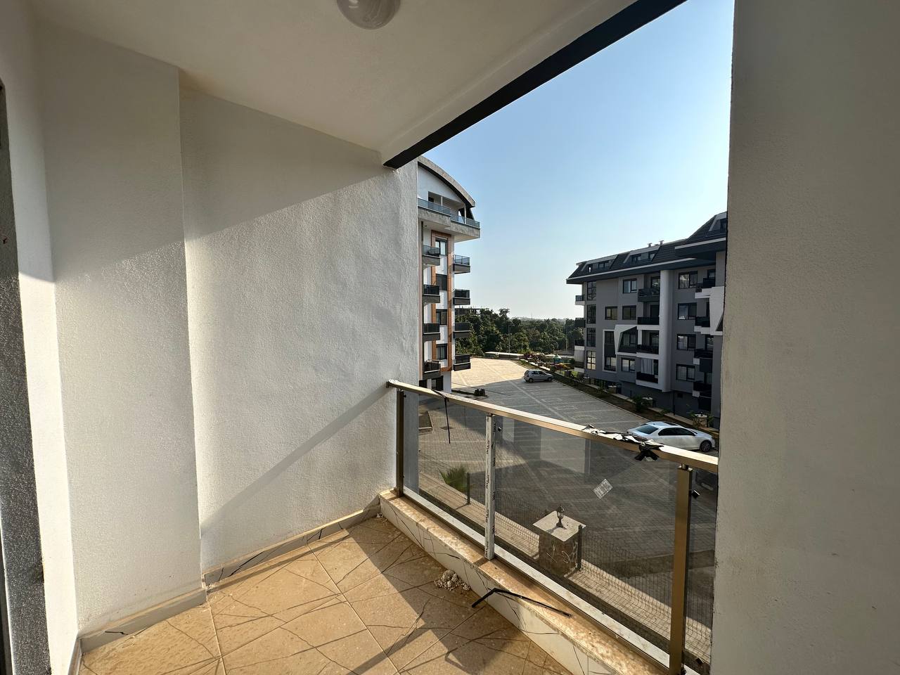 Dokulu beyaz duvarlı kapalı balkon, Türkiye’de taş döşeli iç yol ve park edilmiş araçlara bakıyor