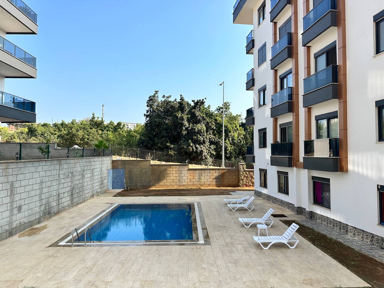 Metal merdivenli açık yüzme havuzu, Alanya’daki 2+1 dairelerin bulunduğu rezidansta beyaz şezlonglarla
