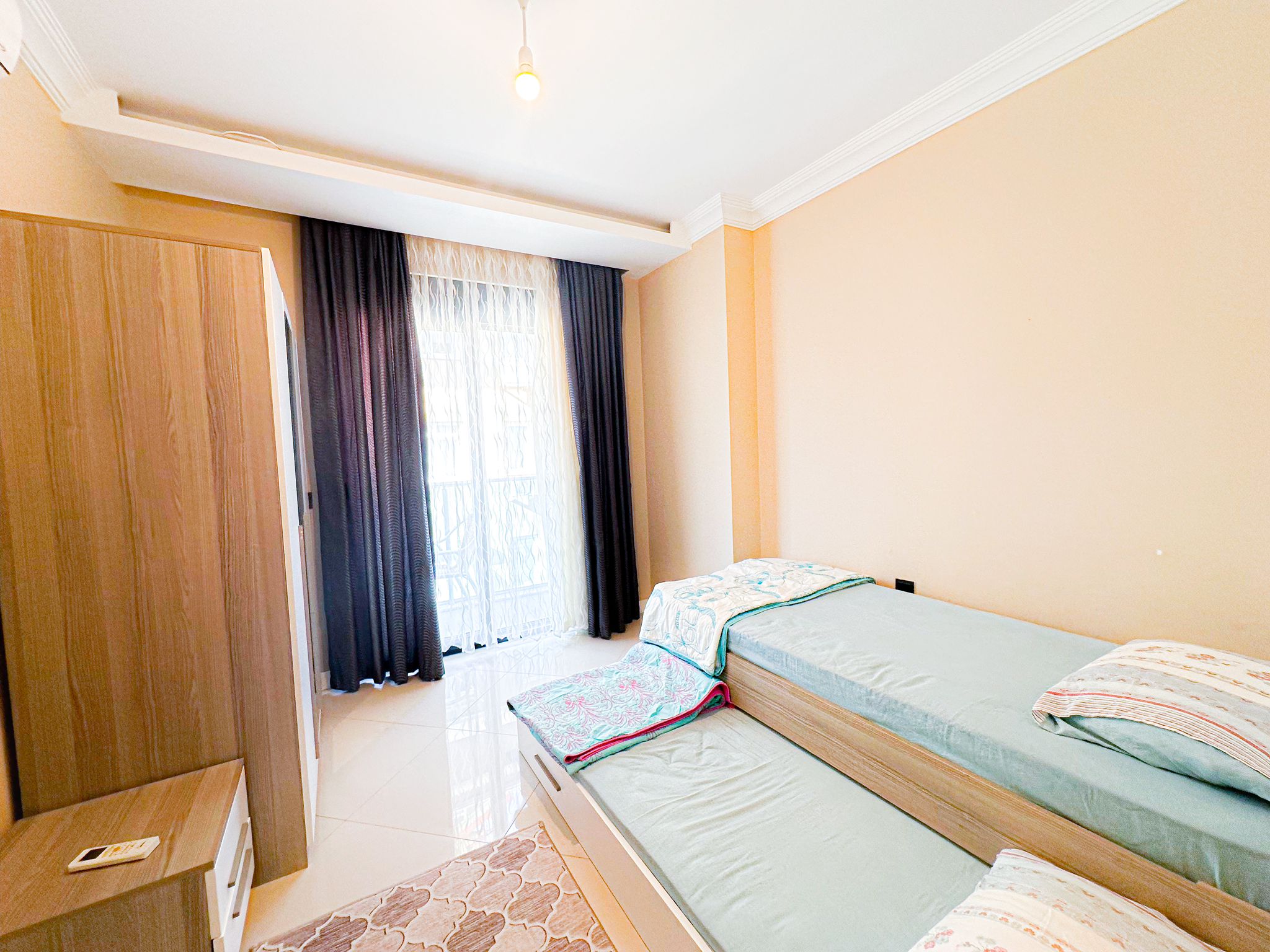 İki tek kişilik yataklı yatak odası, Alanya’daki dairenin ahşap dolabı ve balkon kapısıyla