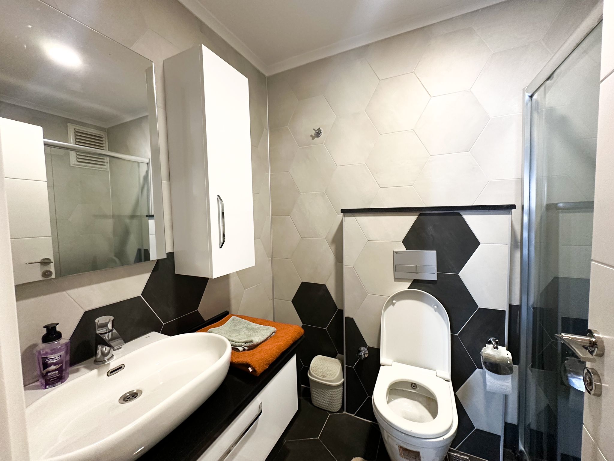 Duş kabinli banyo, Alanya’daki konutun siyah tezgâhı ve duvar aynasıyla