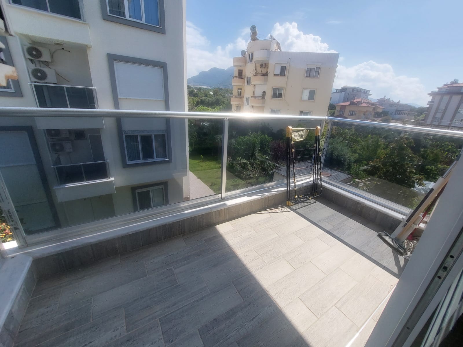 Geniş teras cam korkuluk ve uzaktaki dağ siluetiyle satıştaki konuta açılıyor