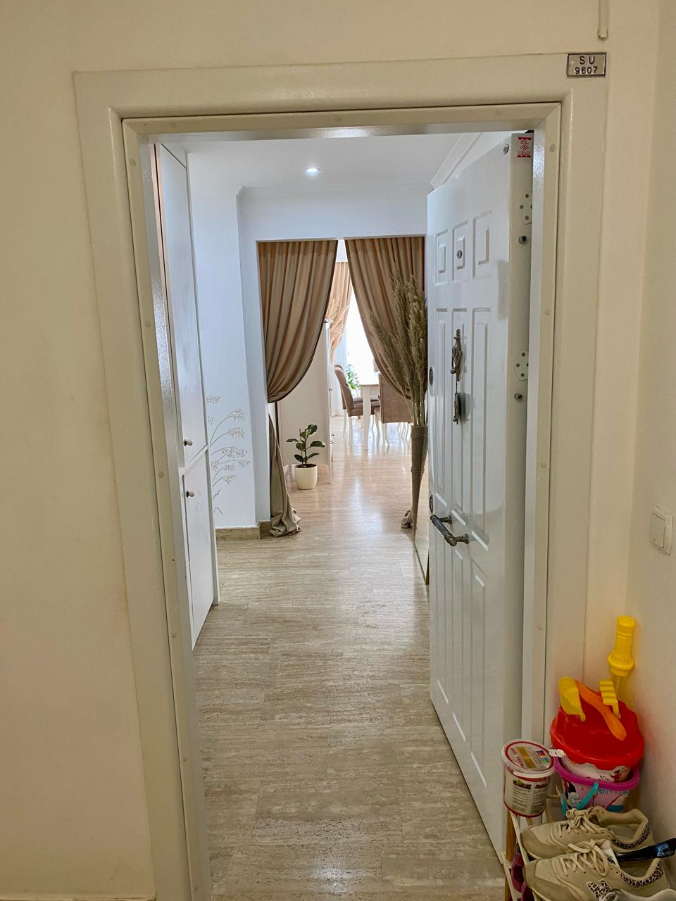 Alanya’daki 2+1 dairenin antre bölümünde açık beyaz kapı, dolap ve saksı bitkisi