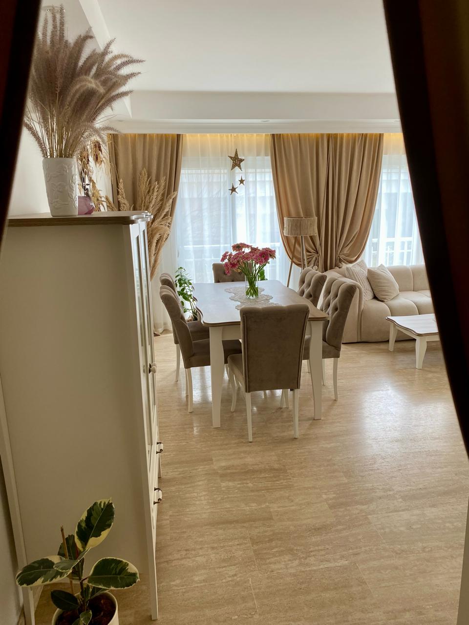 Oba’daki dairenin mutfaklı salonunda bej kanepe, yemek masası ve tüllü panoramik pencereler