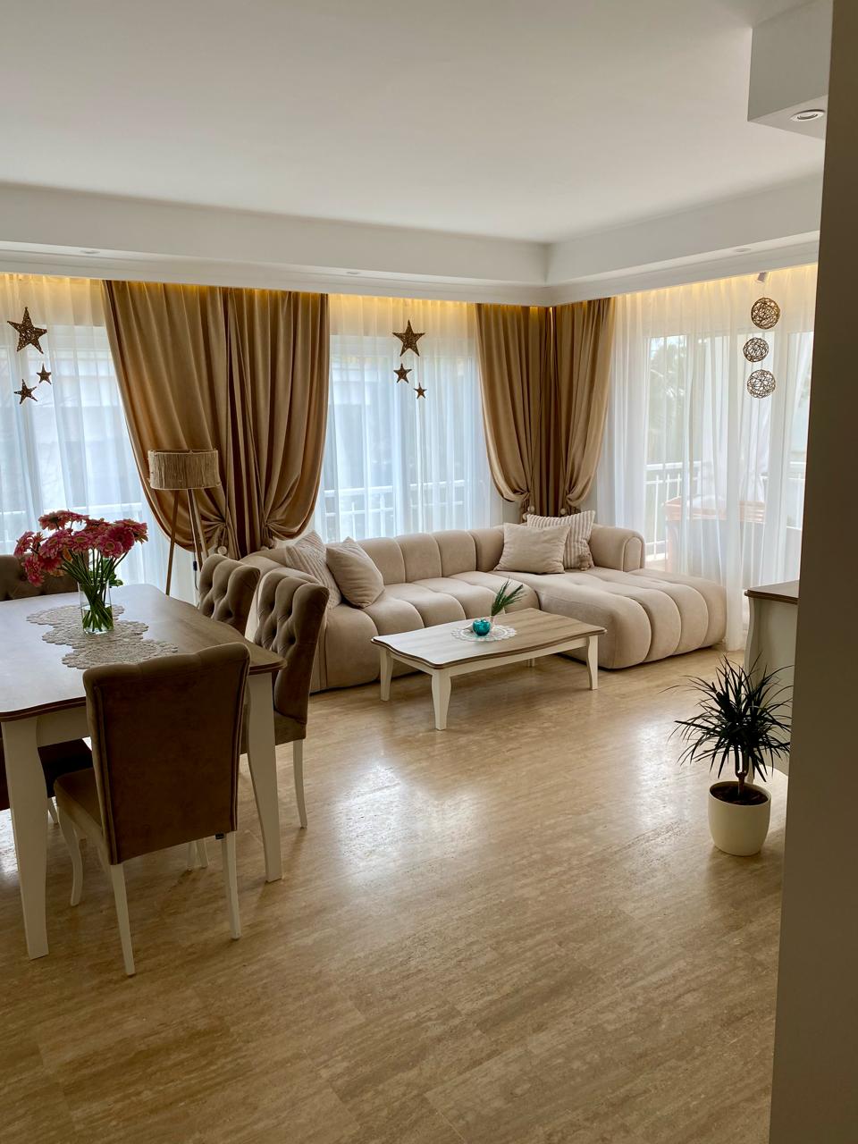 Alanya’da satılık konutun mutfaklı salonunda bej köşe kanepe ve panoramik pencereler