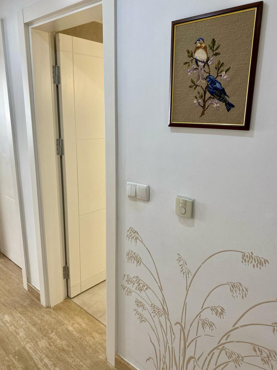 Oba’daki dairenin koridorunda açık beyaz iç kapı, başak desenli duvar ve kuşlu tablo
