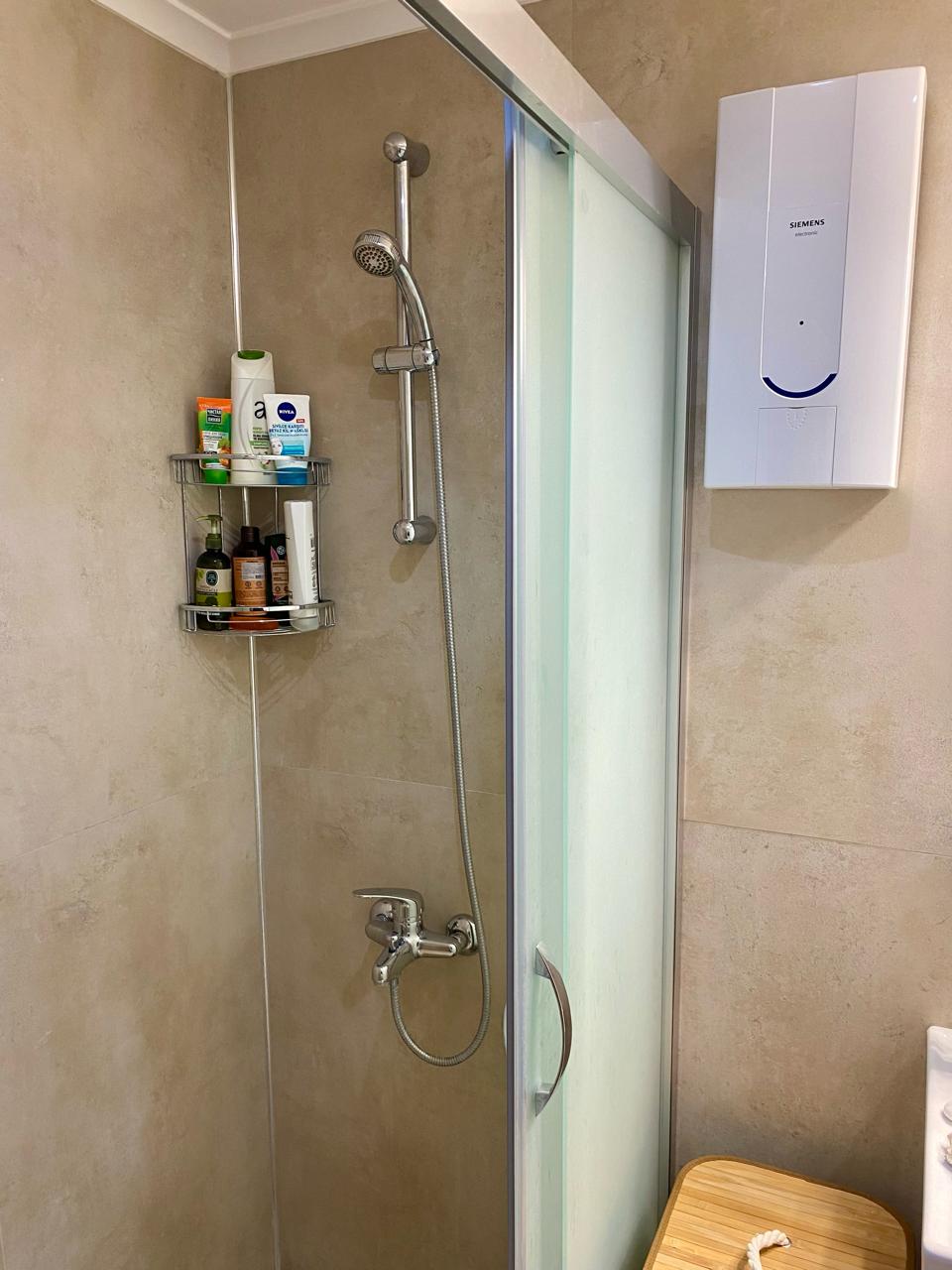 Oba’daki banyoda krom duş sistemi, kozmetik rafları ve mat camlı duş kabini