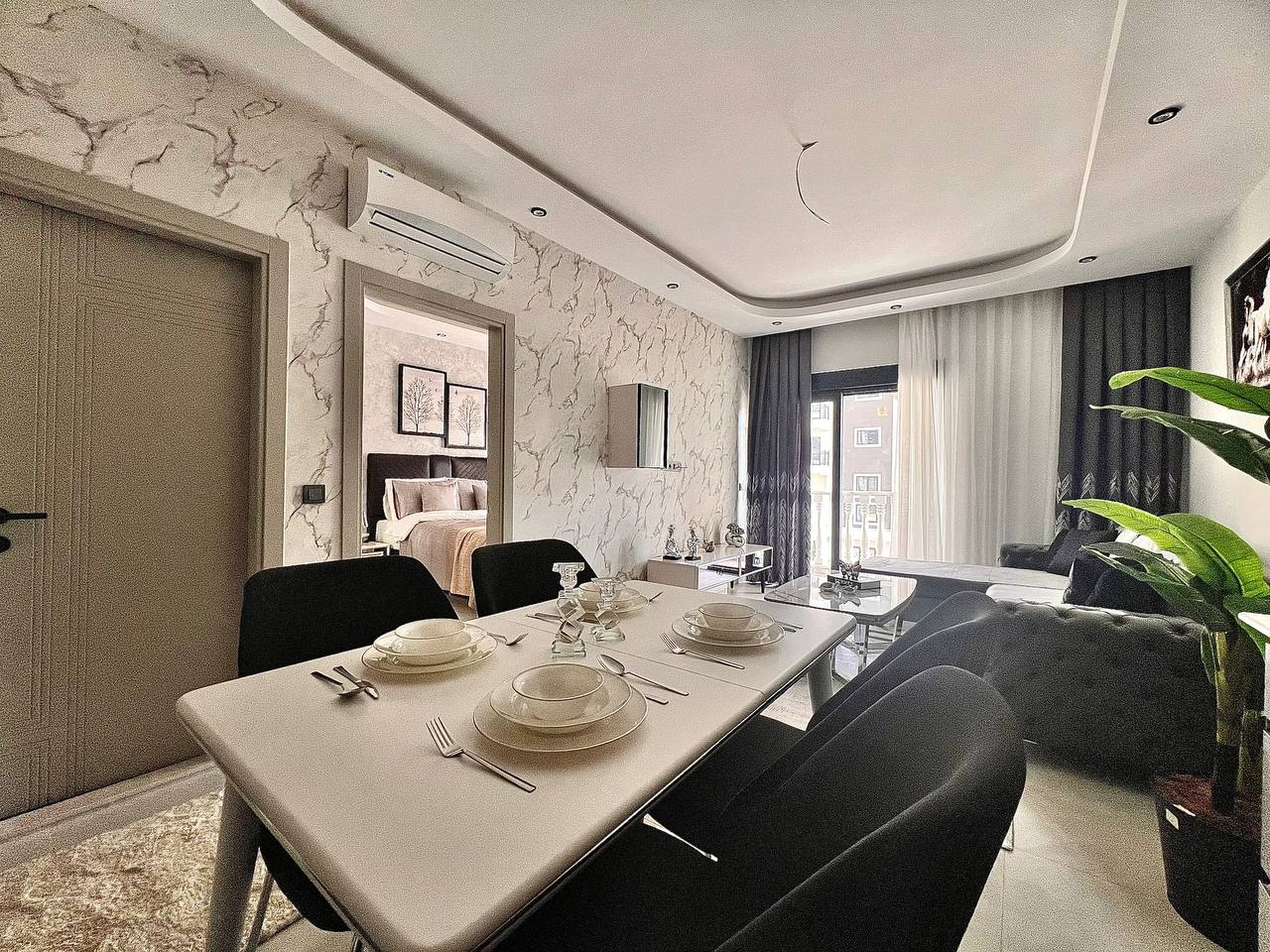 Satılık 1+1 dairenin mutfaklı salonunda servisli yemek masası ve gri köşe koltuk