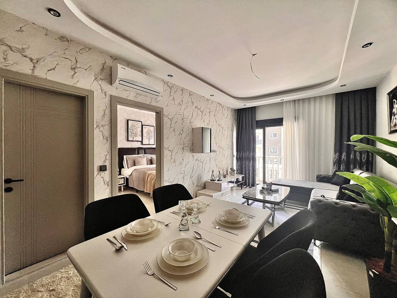 Alanya Türkiye’deki 1+1 dairenin salonunda servisli masa, gri koltuk ve balkon kapısı