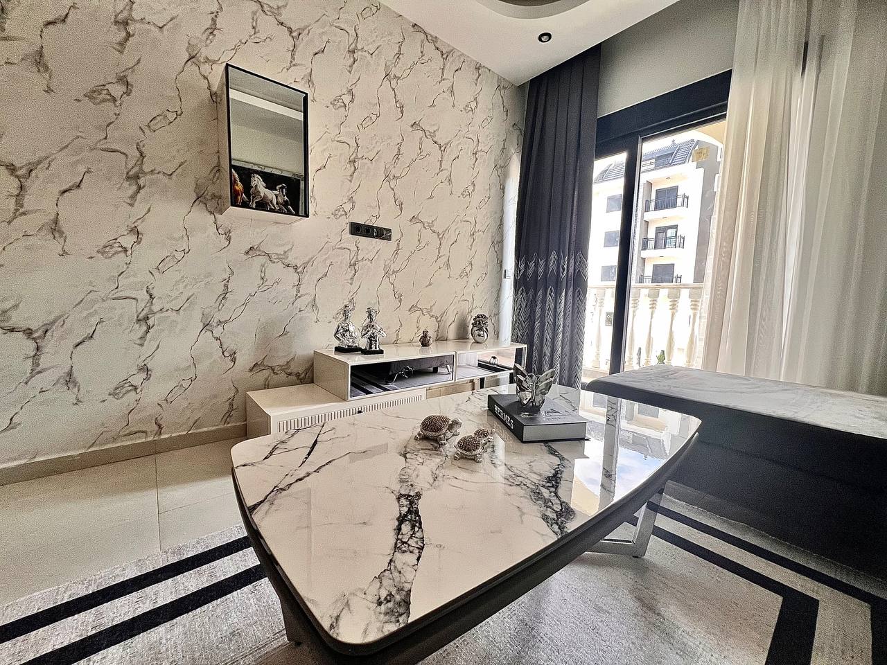 Türkiye’de satılık konutun salonunda mermer sehpa, gri köşe koltuk ve balkon kapısı