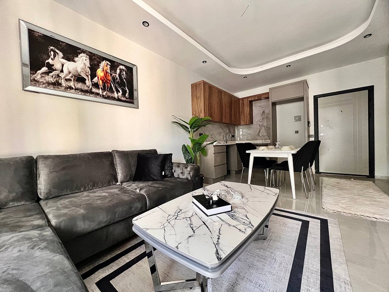 Satılık 1+1 dairenin mutfaklı salonunda gri koltuk ve dalgalı tavan nişi