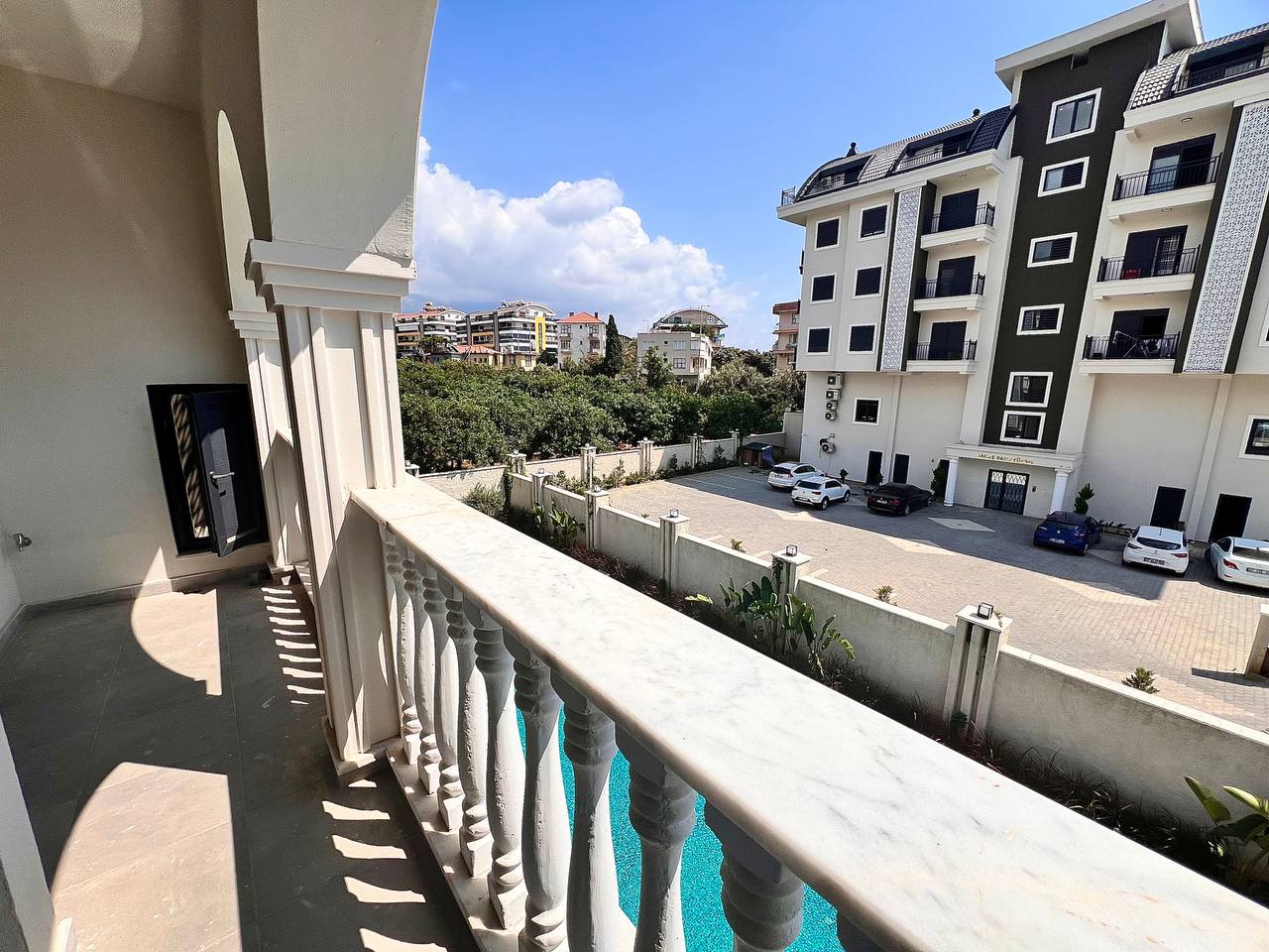 Oba’daki 1+1 dairenin uzun balkonunda mermer korkuluk, otopark ve havuz manzarası