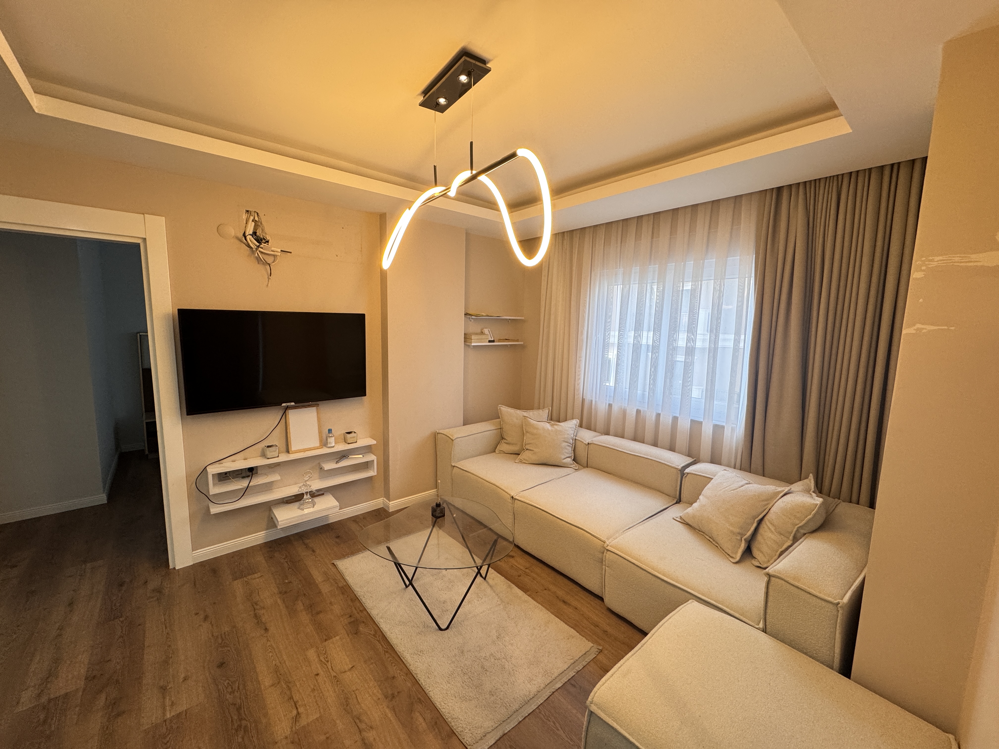 Bej köşe kanepeli salon Türkiye'de, duvar tipi televizyon ve cam sehpayla düzenlenmiş