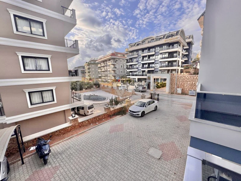 Taş döşeli araç yolunda, Türkiye'de satılık dairelerin bulunduğu sitenin balkonlu cepheleri ve giriş kapısı