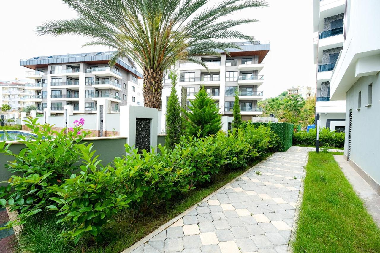 Paved walkway with a palm and flowering shrubs on the grounds of a residence with flats in Oba