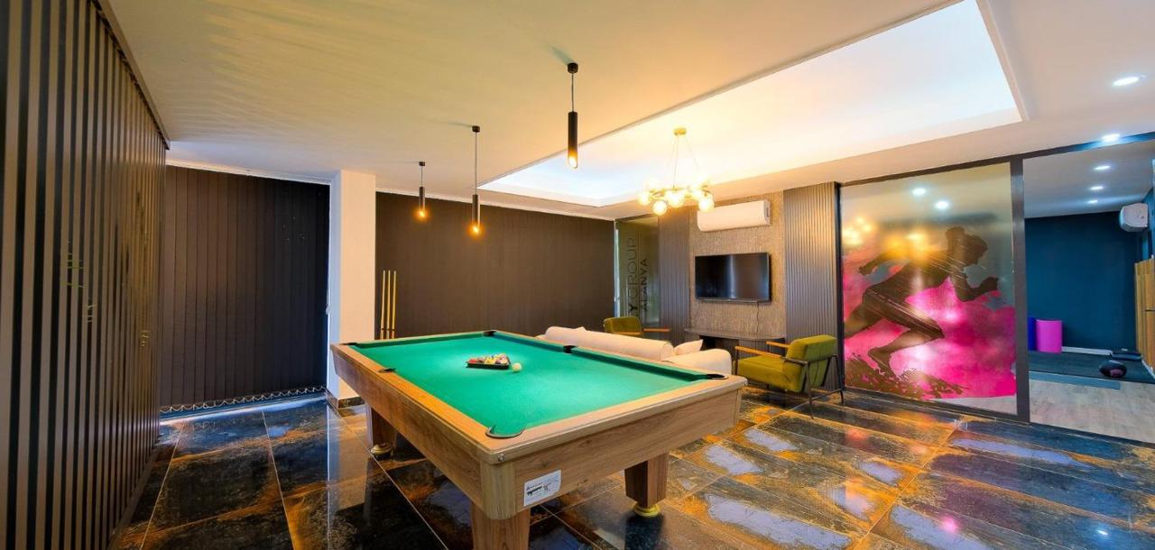 Billiards room with a green-felt table, soft armchairs, and dark slatted walls for apartment residents