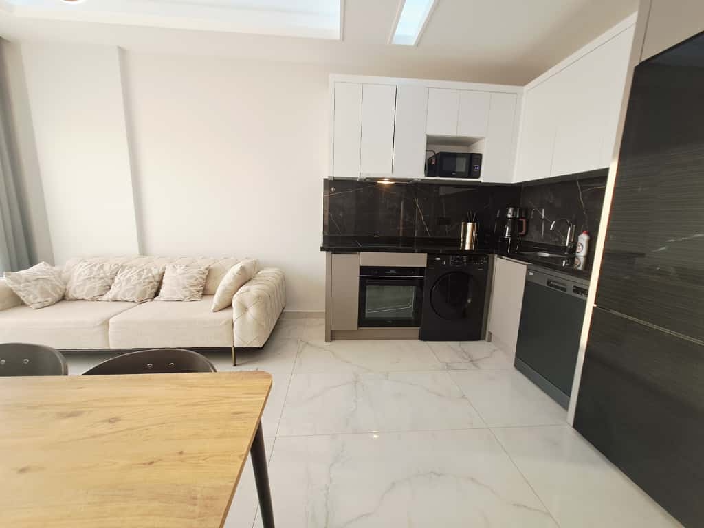 Kitchen-living room with white cabinets, black marble counters, and a dining table in a 1+1 apartment