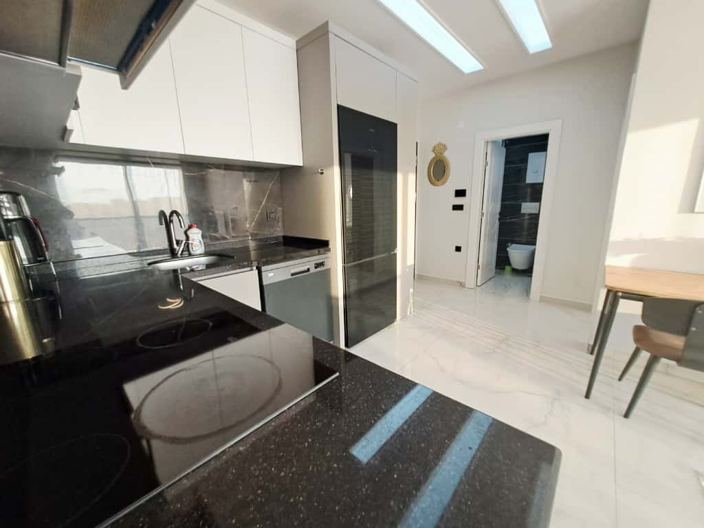 Kitchen with a black countertop, white upper cabinets, and a dining table in an apartment in Oba