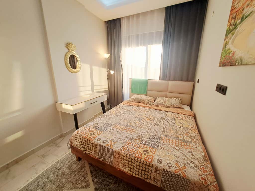 Bedroom with a double bed, beige upholstered headboard, and gray blackout curtains in a flat