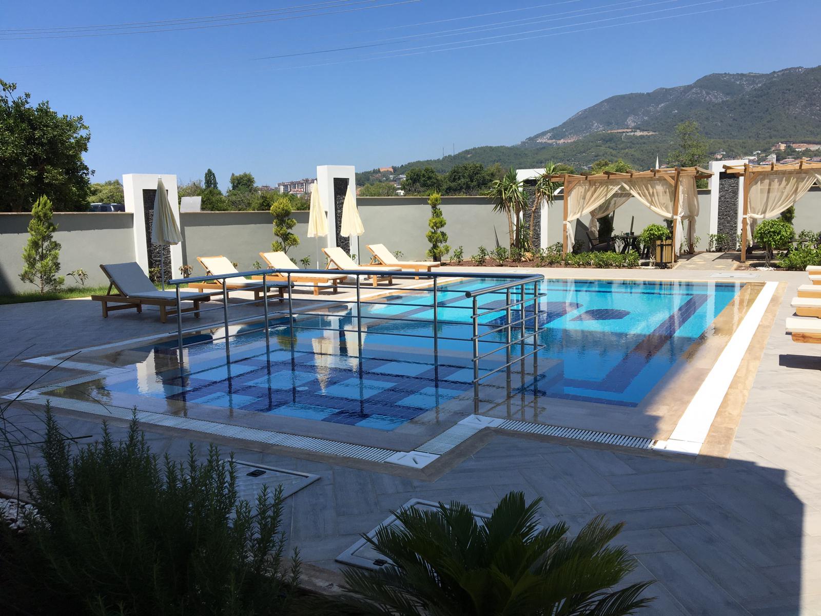 Blue pool with white loungers and curtained gazebos in a complex with apartments in Oba
