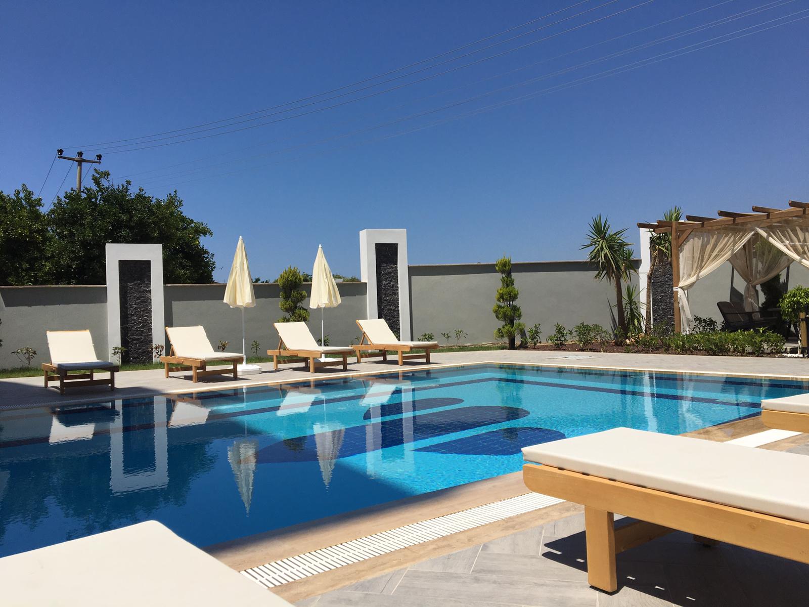 Pool with a dark mosaic pattern and wooden loungers in Turkey, where homes are for sale