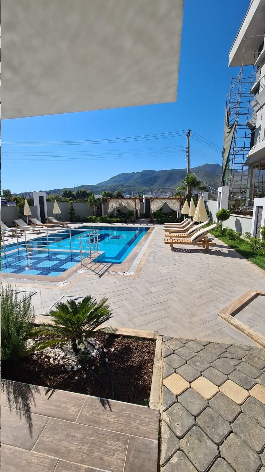 Rectangular pool with curtained gazebos by residential buildings in Alanya, where flats are for sale