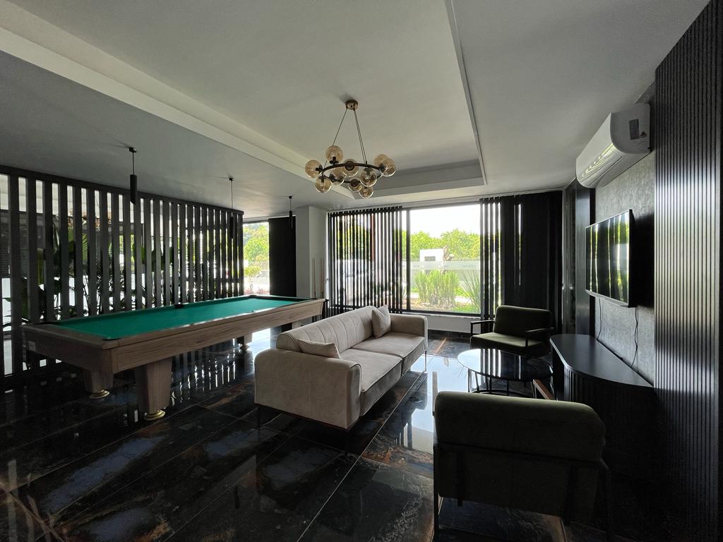 Billiards room with a green-felt table, light sofa, and panoramic windows with blinds in Oba