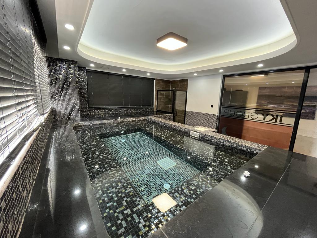 Indoor pool with black and gray mosaic walls and dark stone edges for apartment residents