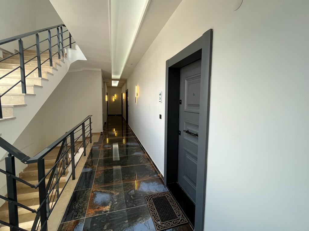 Stair hall with beige stone steps, black metal railings, and a dark glossy tile floor for apartment residents