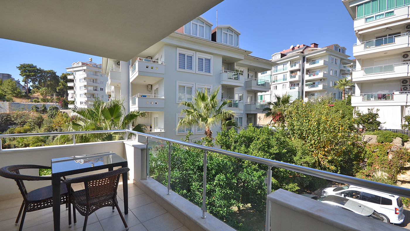 Cam korkuluklu balkon ve yeşillikler arasındaki masa, satılık dairede
