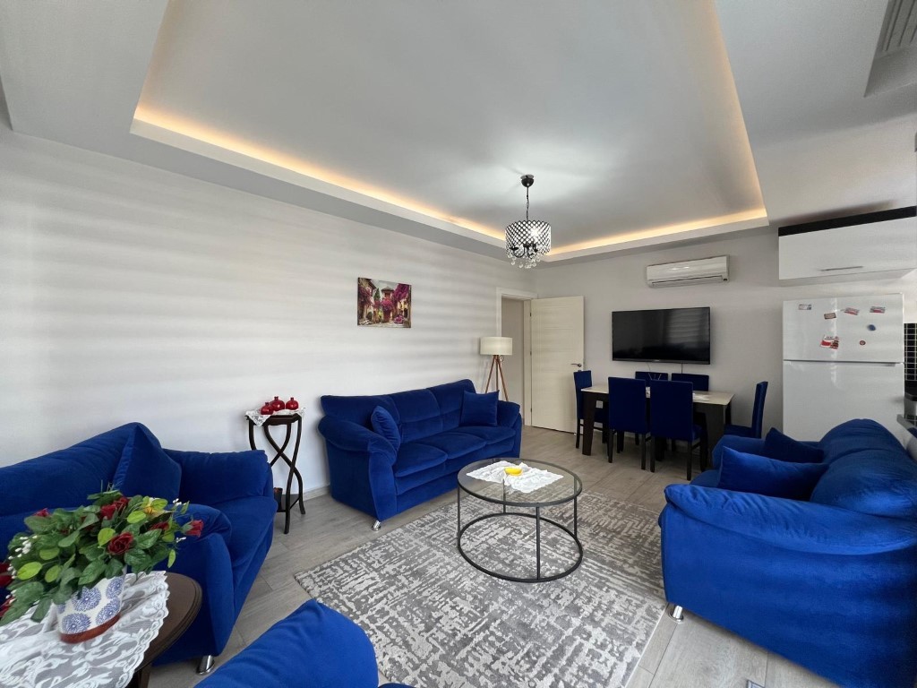 Mavi koltuklu salon, yemek masası ve geometrik halı Kestel’de satılık konutun yaşam alanını gösteriyor