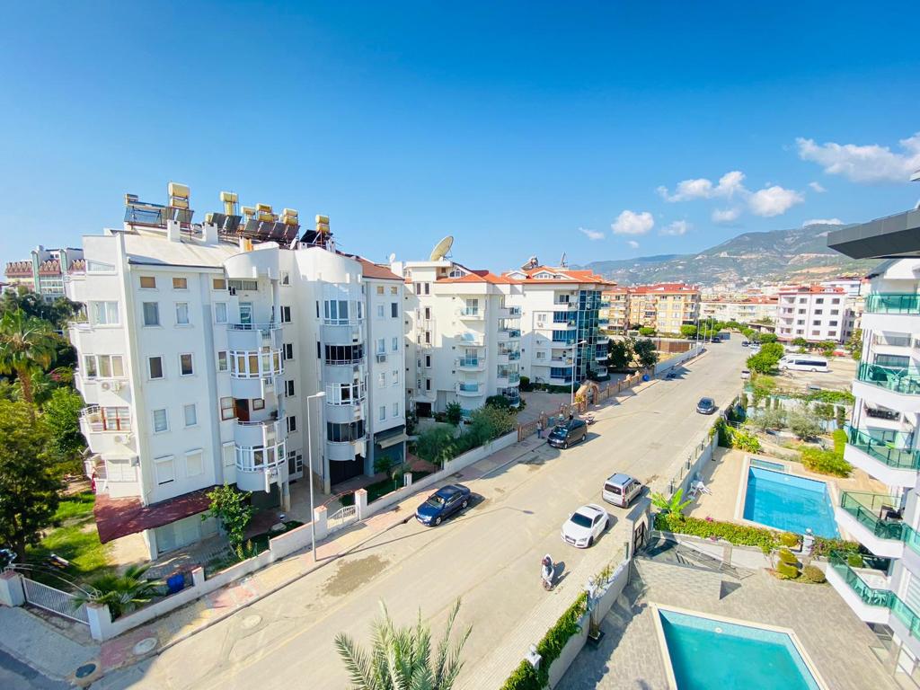Güneşli gökyüzü altında şehir caddesi, Oba’da avlu havuzu ve dağ manzarasıyla