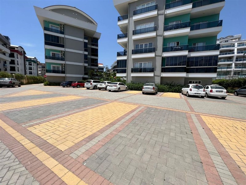 Park edilmiş araçların bulunduğu açık otopark ve koyu balkonlu binalar