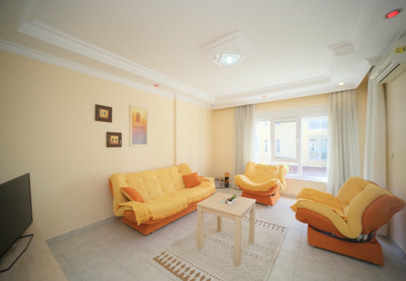 Sarı koltuk ve berjerlerin bulunduğu salonda geniş pencere önündeki satılık daire düzeni görülüyor