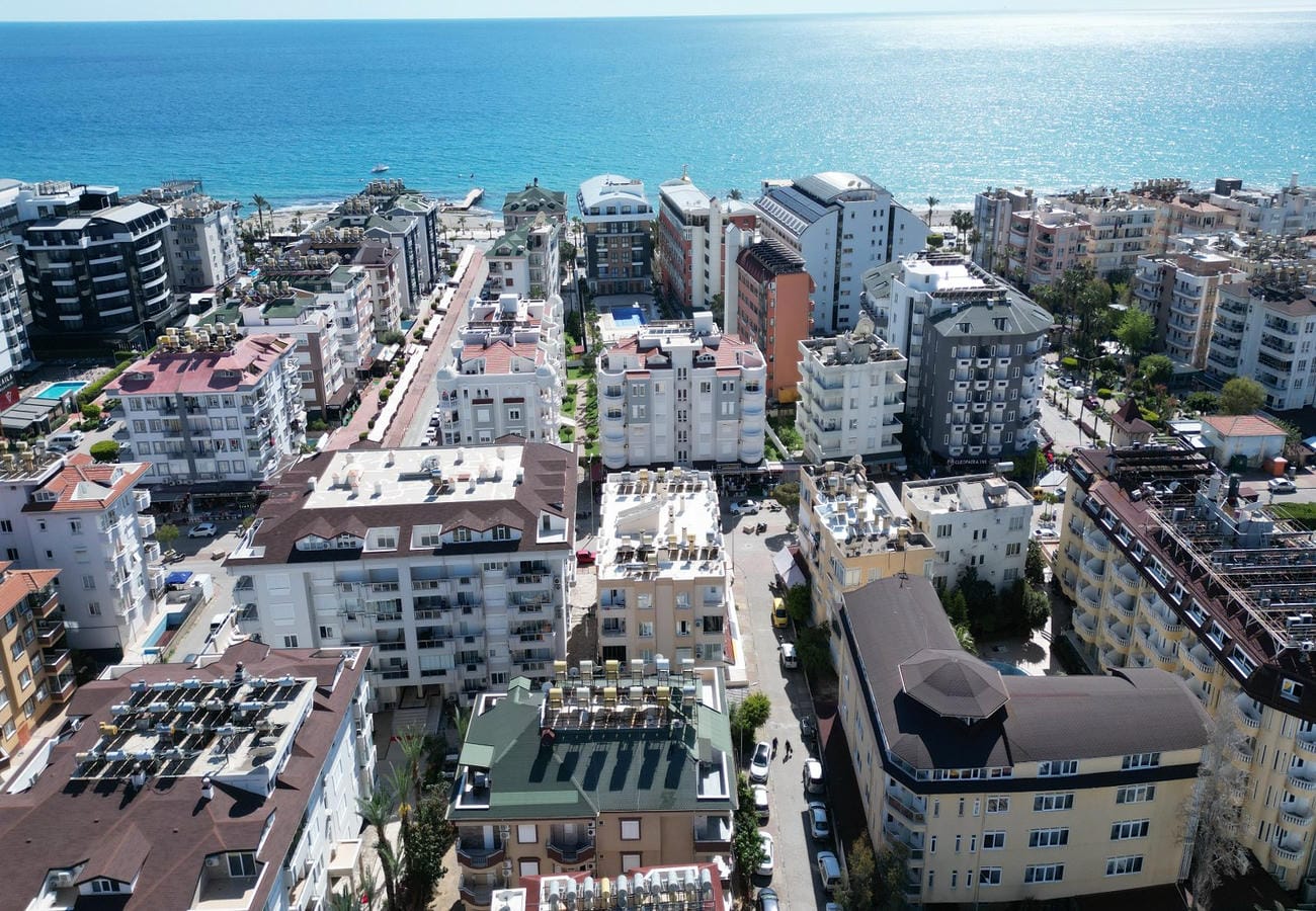 Güneşli deniz yüzeyi ve renkli cepheli yapılarla çevrili kıyı Oba’da Türkiye’deki daireleri gösteriyor