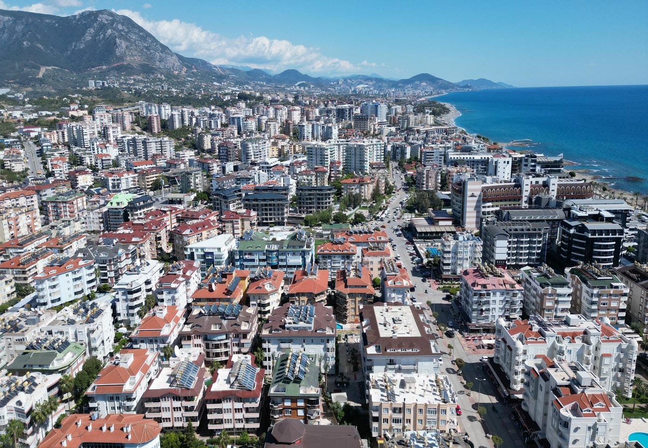 Mavi deniz ve dağlarla çevrili kıyı panoramasında Türkiye’de satışta olan rezidanslar ve kırmızı çatılar görülüyor