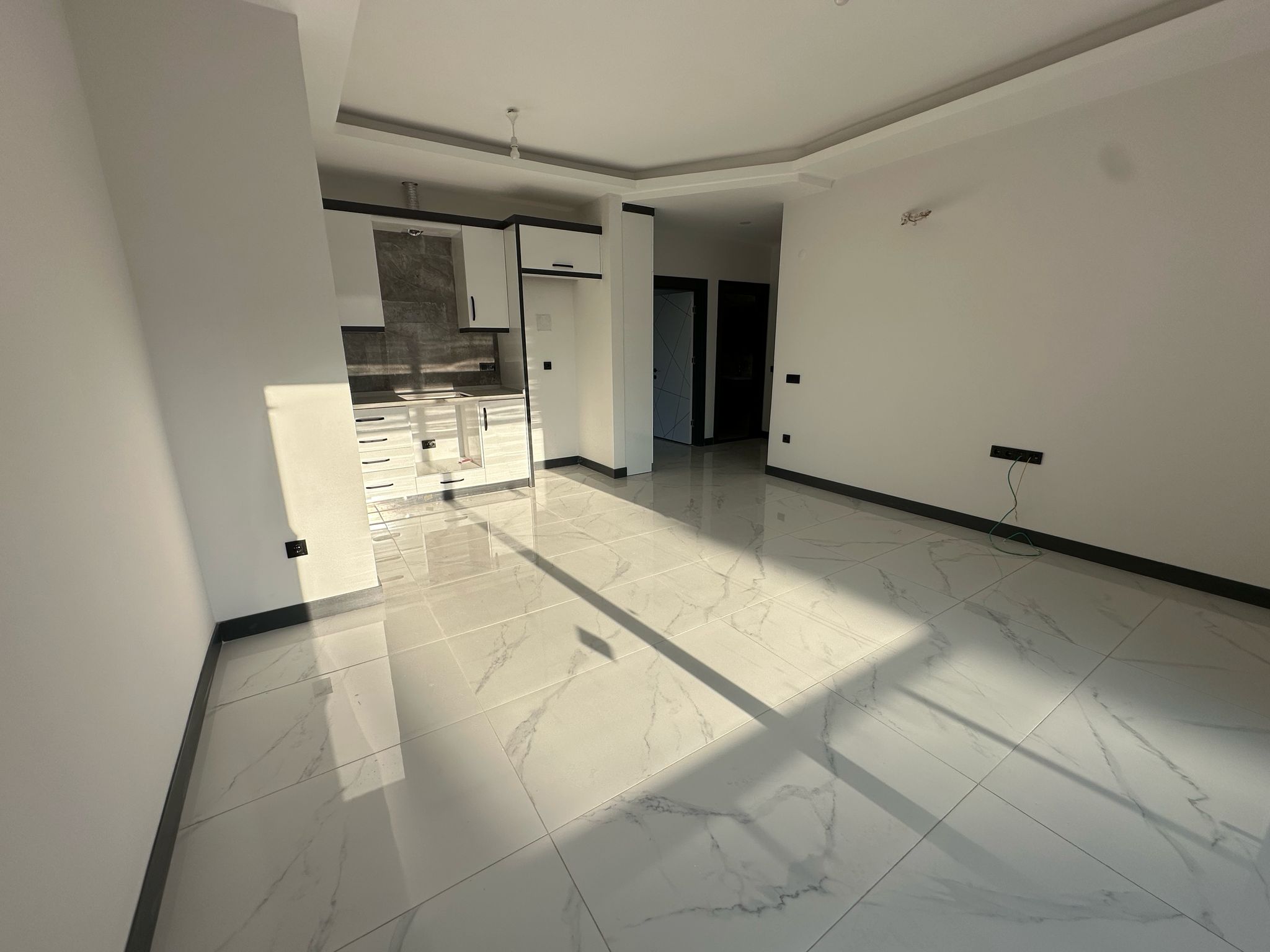 Beyaz mutfak ünitesi ve boş salon alanı, Türkiye’deki konutun mutfak-salonunda