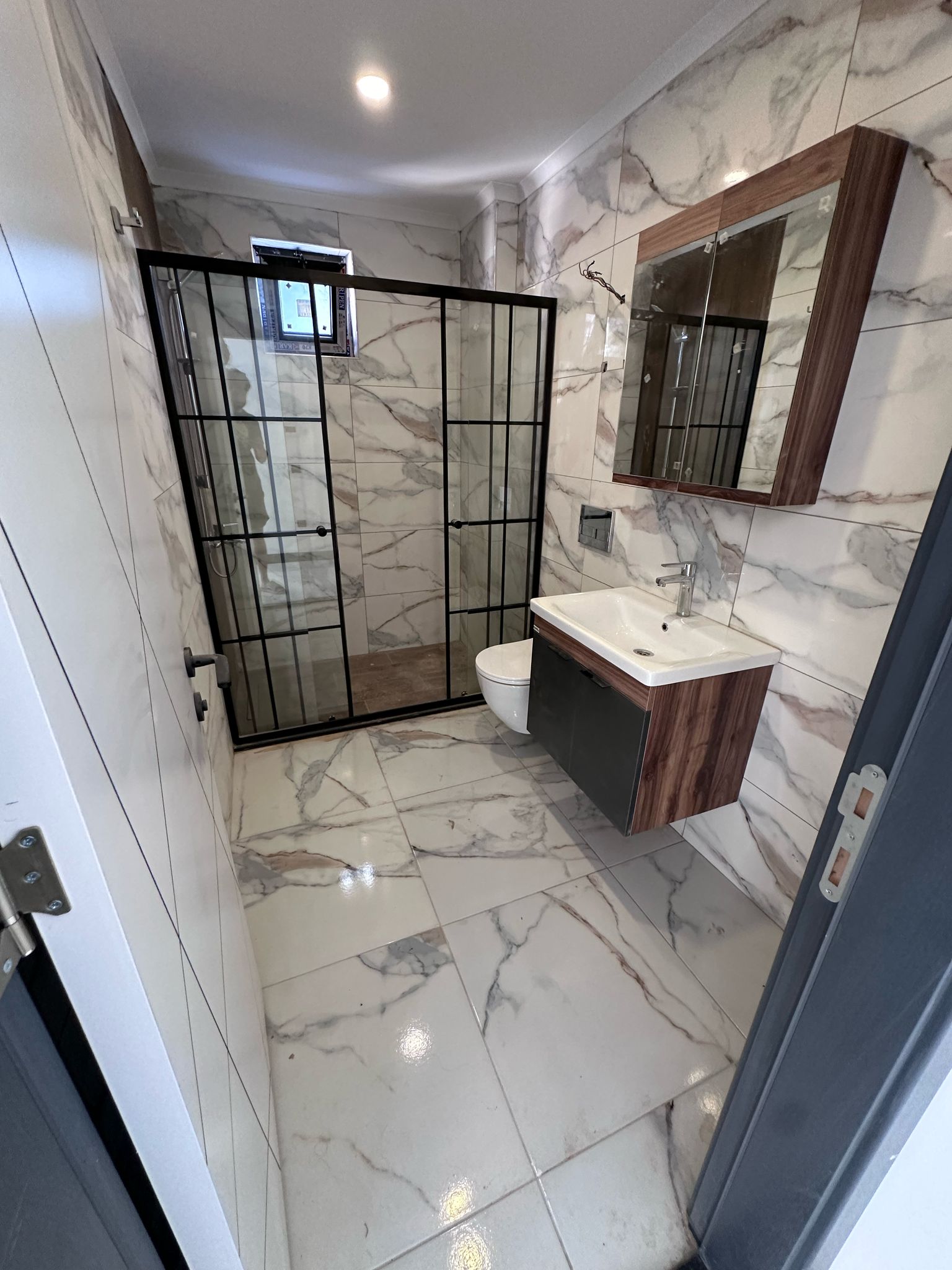 Siyah çerçeveli cam duş kabinli banyo, Oba’daki dairenin mermer desenli banyosunda